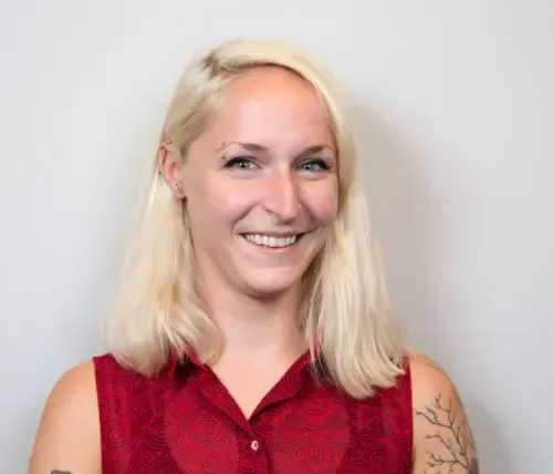 Blonde woman smiling, wearing a red sleeveless top, with a light background.