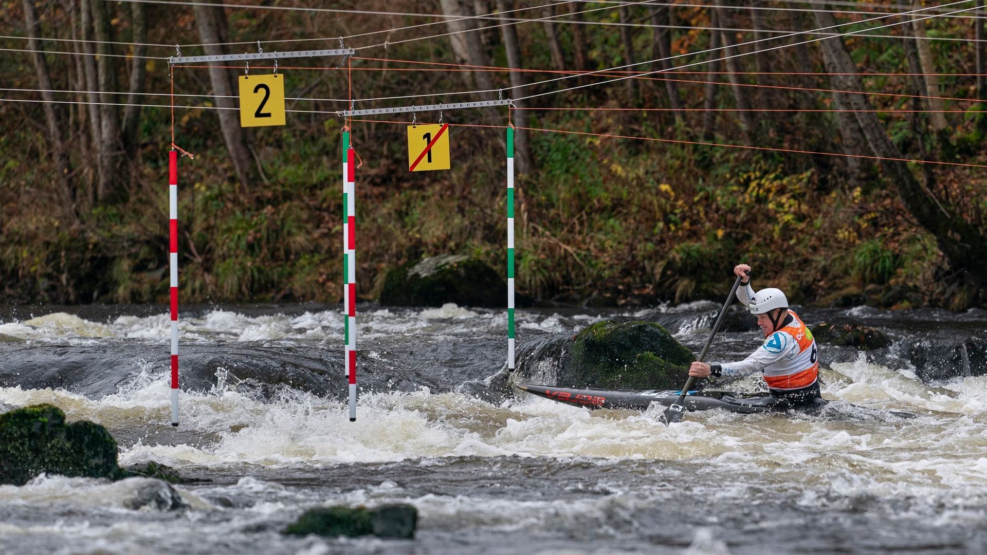 Canoe slalom competitor navigates a rapid course through gates marked with red/green/white poles and the number 2, with a yellow cross-out gate.
