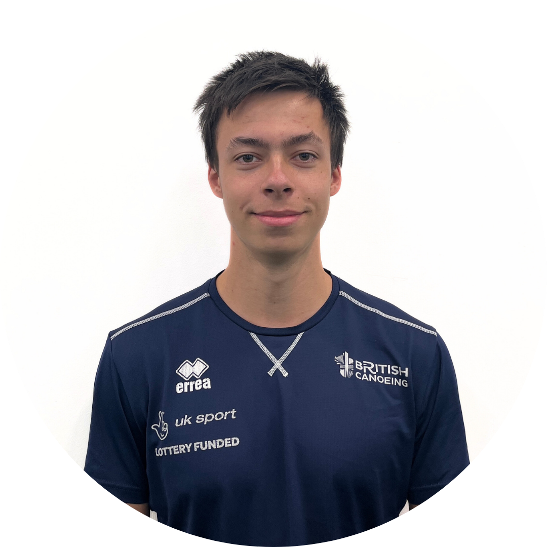 A young man with short dark hair wearing a navy shirt with logos, smiling in front of a white background.