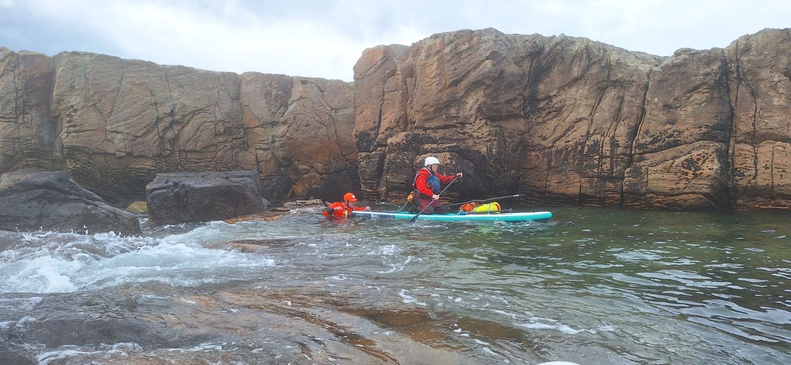A group of people are riding kayaks in the water near a rocky shoreline.