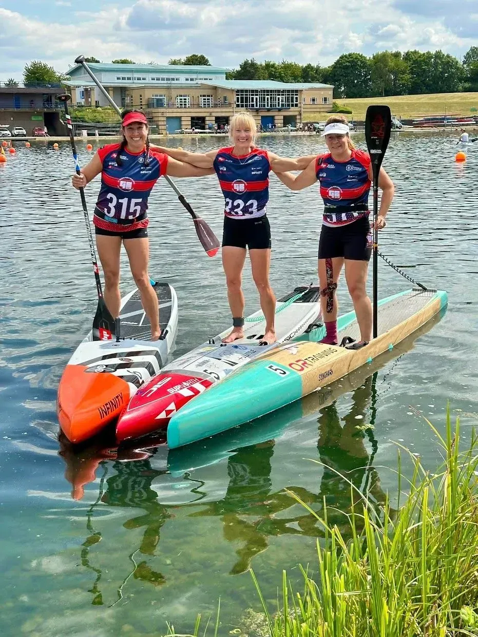 Three people are standing on kayaks in the water.