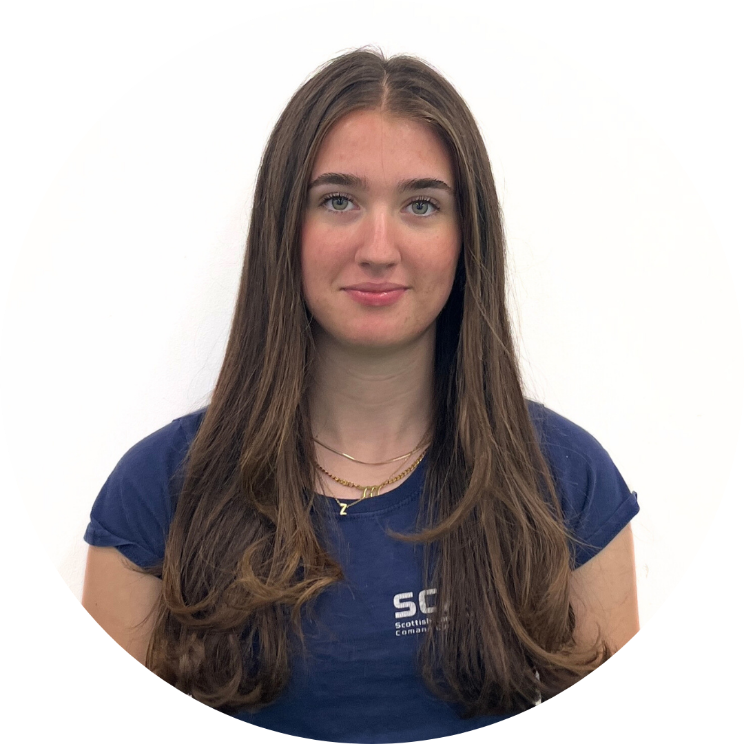 Young woman with long brown hair wearing a blue shirt, smiling at the camera. White background.