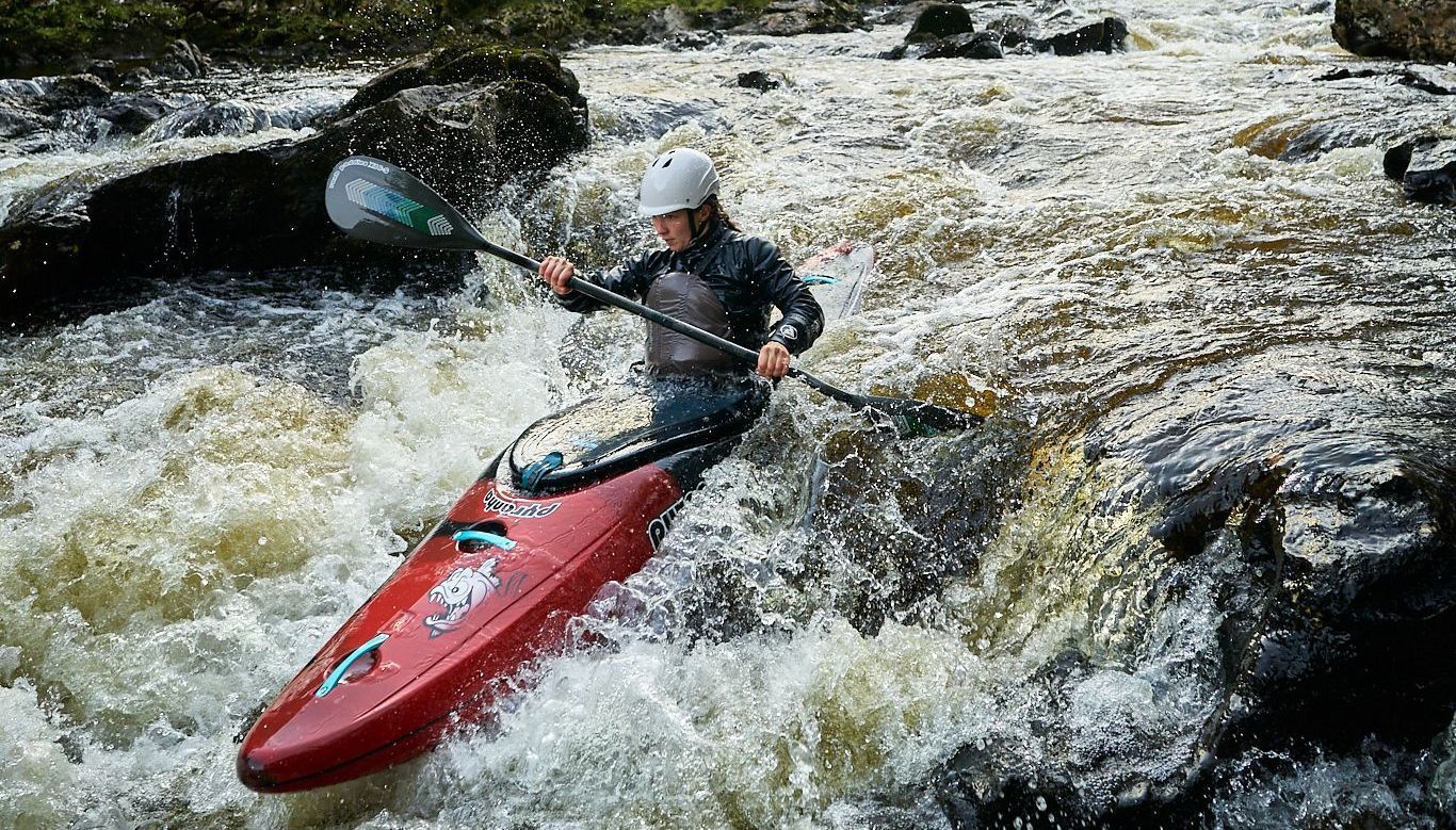 A person is paddling a red kayak through a river.