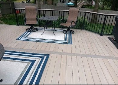 Patio deck with two chairs and a round table on blue-patterned outdoor rugs, overlooking a backyard lawn.
