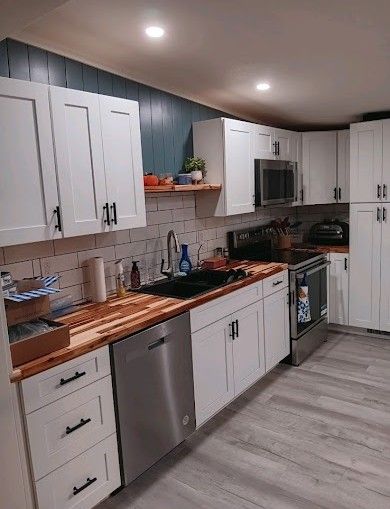 Bright modern kitchen with white cabinets, wood countertops, and stainless steel appliances