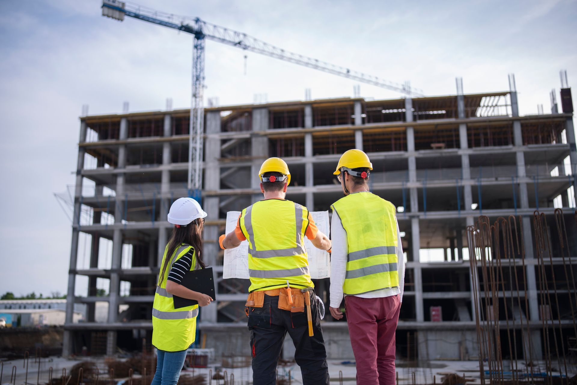 Construction workers reviewing blueprints at a construction site, with a crane and unfinished building in the background.
