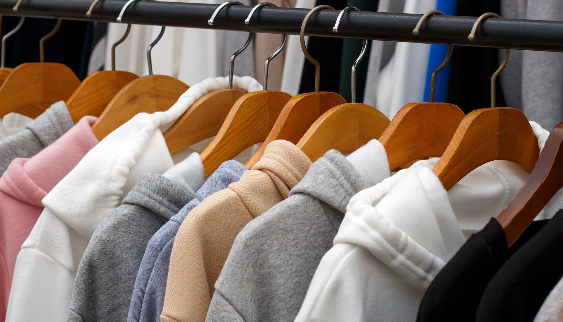 Close-up of a rack of hooded sweatshirts in various neutral colors, hanging on wooden hangers.