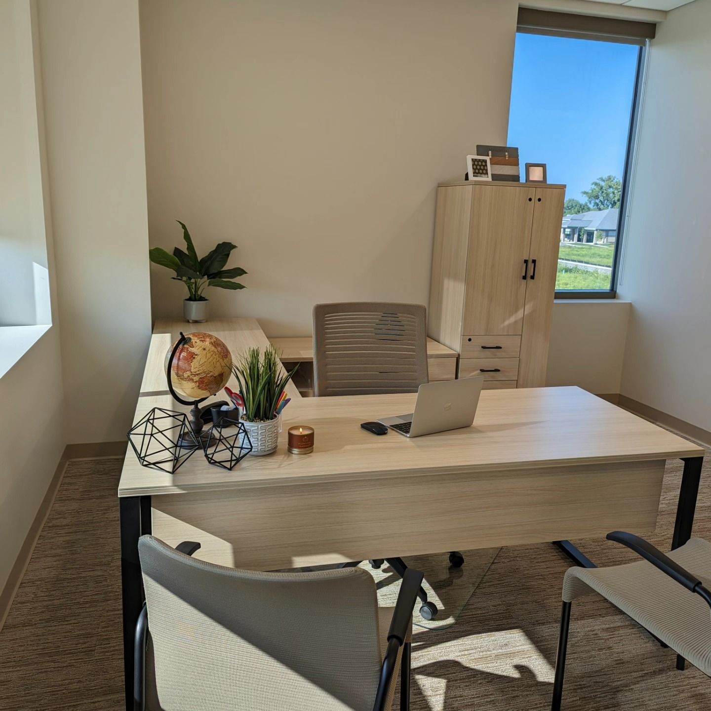 Office desk with laptop, cabinet, chair, globe, and window with a blue sky view.