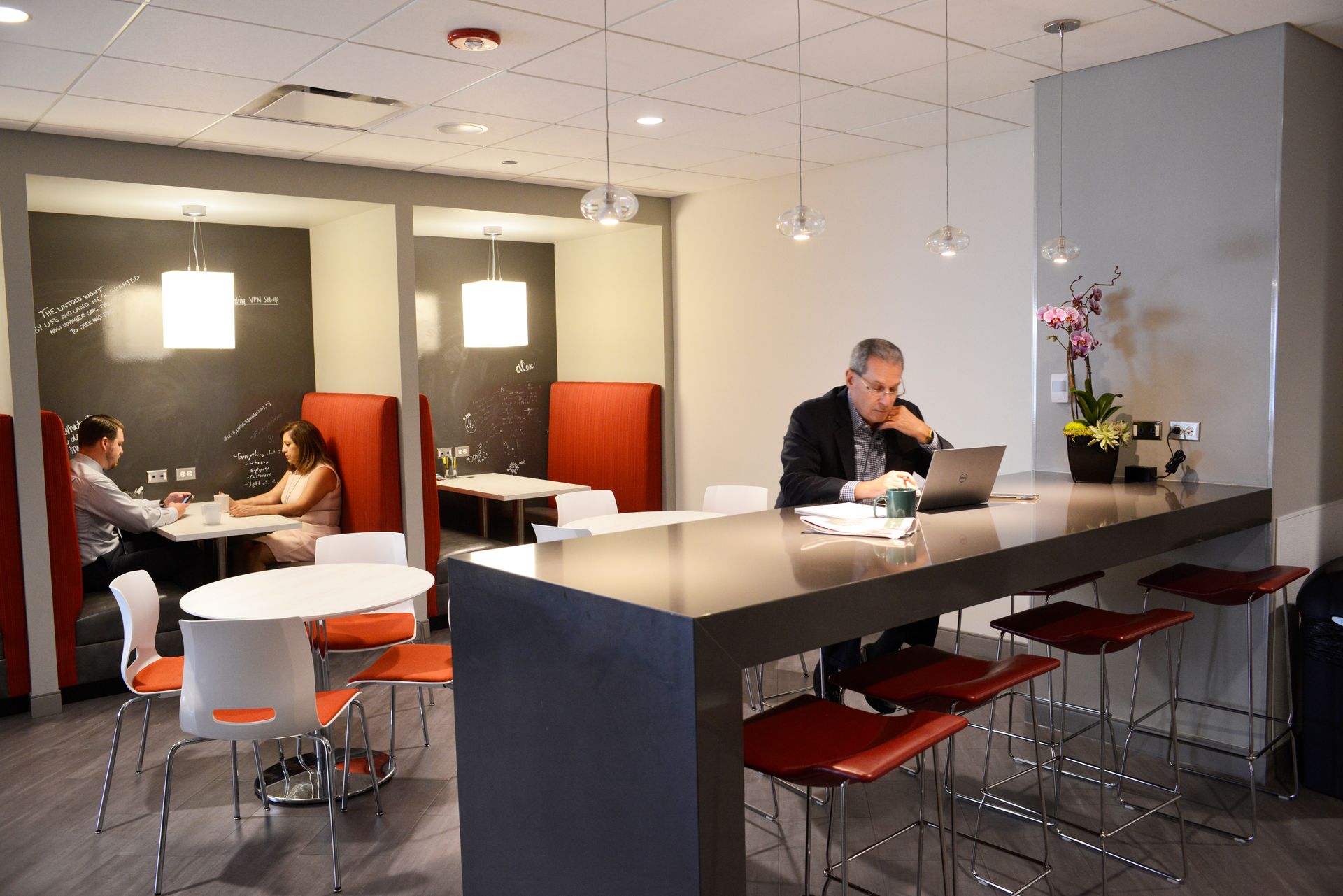 Interior of modern workspace with people working. Tables, chairs, and booths with red accents.