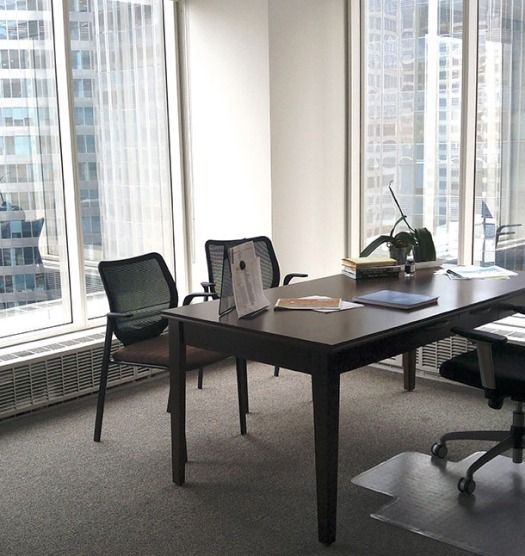 Office with large windows, dark desk, and chairs; city view.