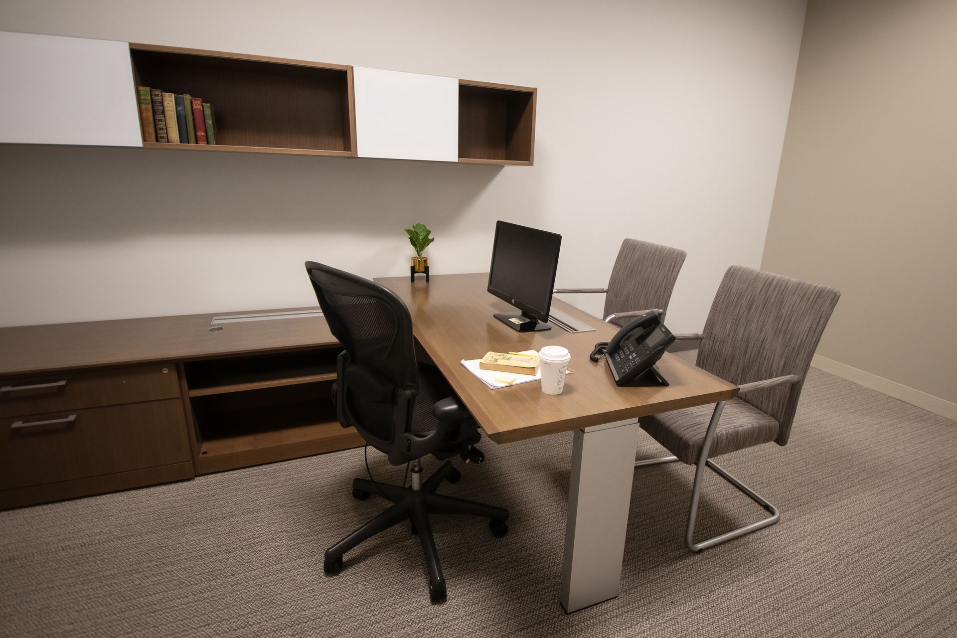 Office with desk, chairs, computer, and built-in storage. Brown and white tones, neutral carpet.