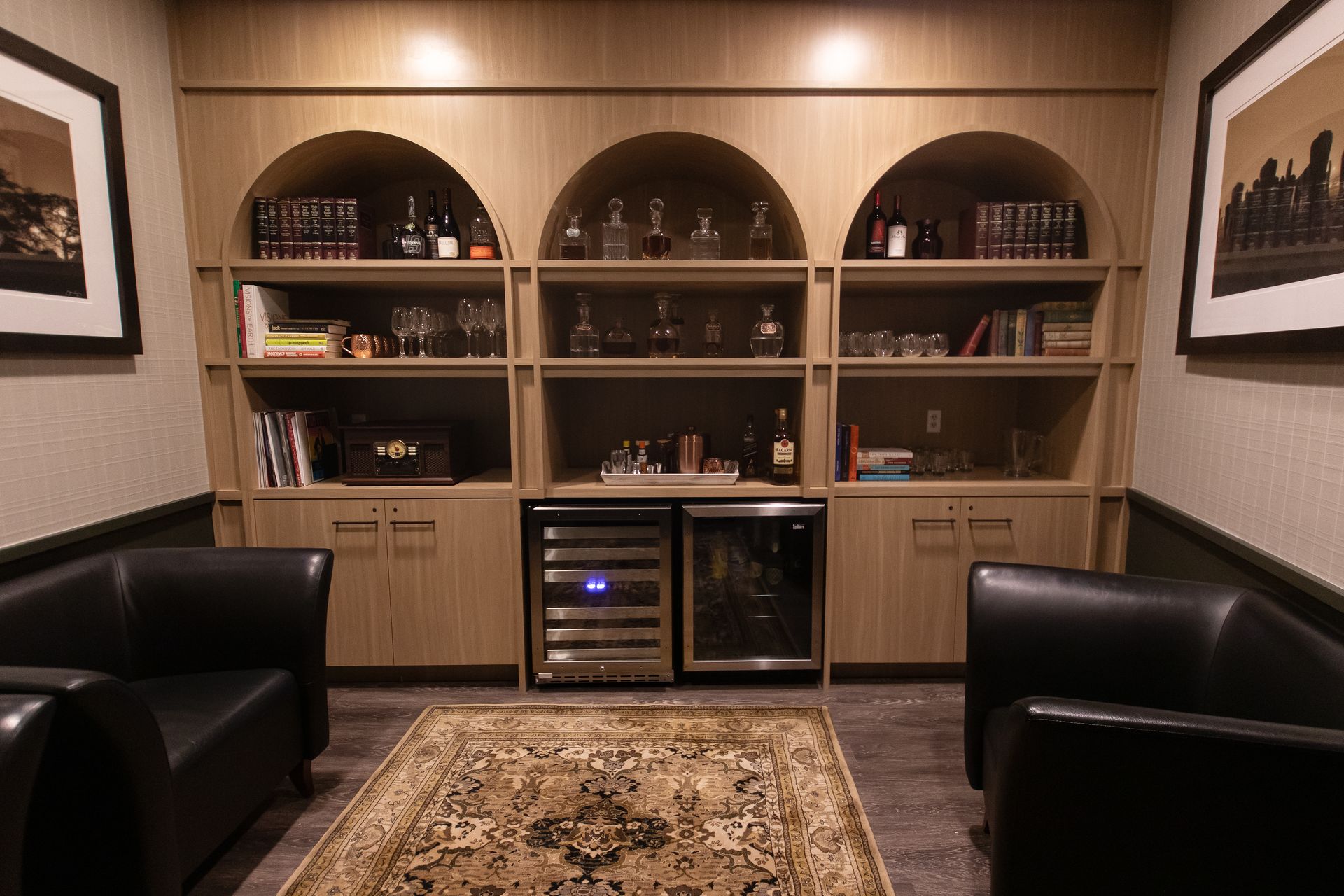 Cozy lounge area with arched bookcase, bar, black leather chairs, and a patterned rug.