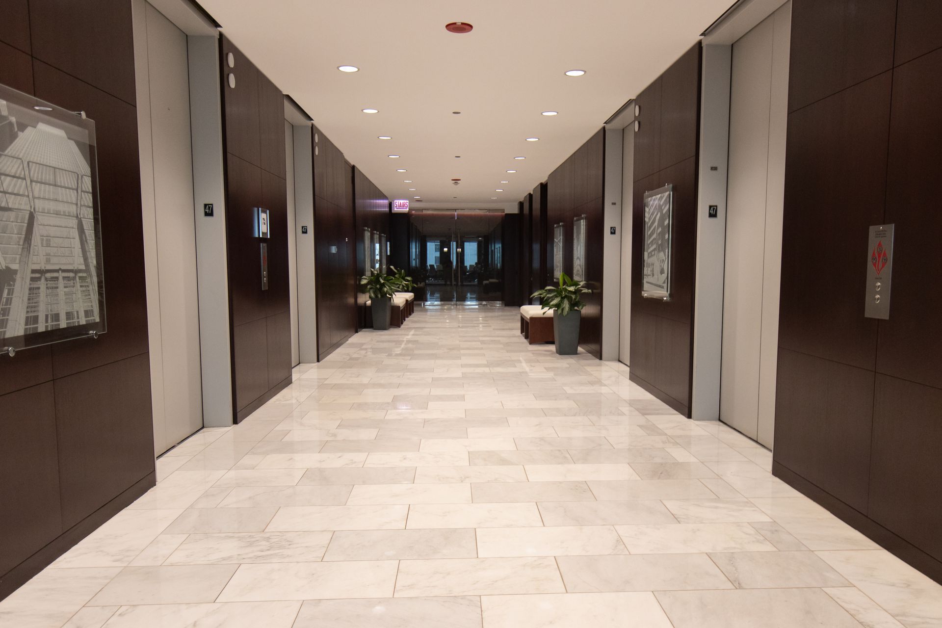 Elevator hallway with brown panel walls, gray doors, marble tile floor, and potted plants.