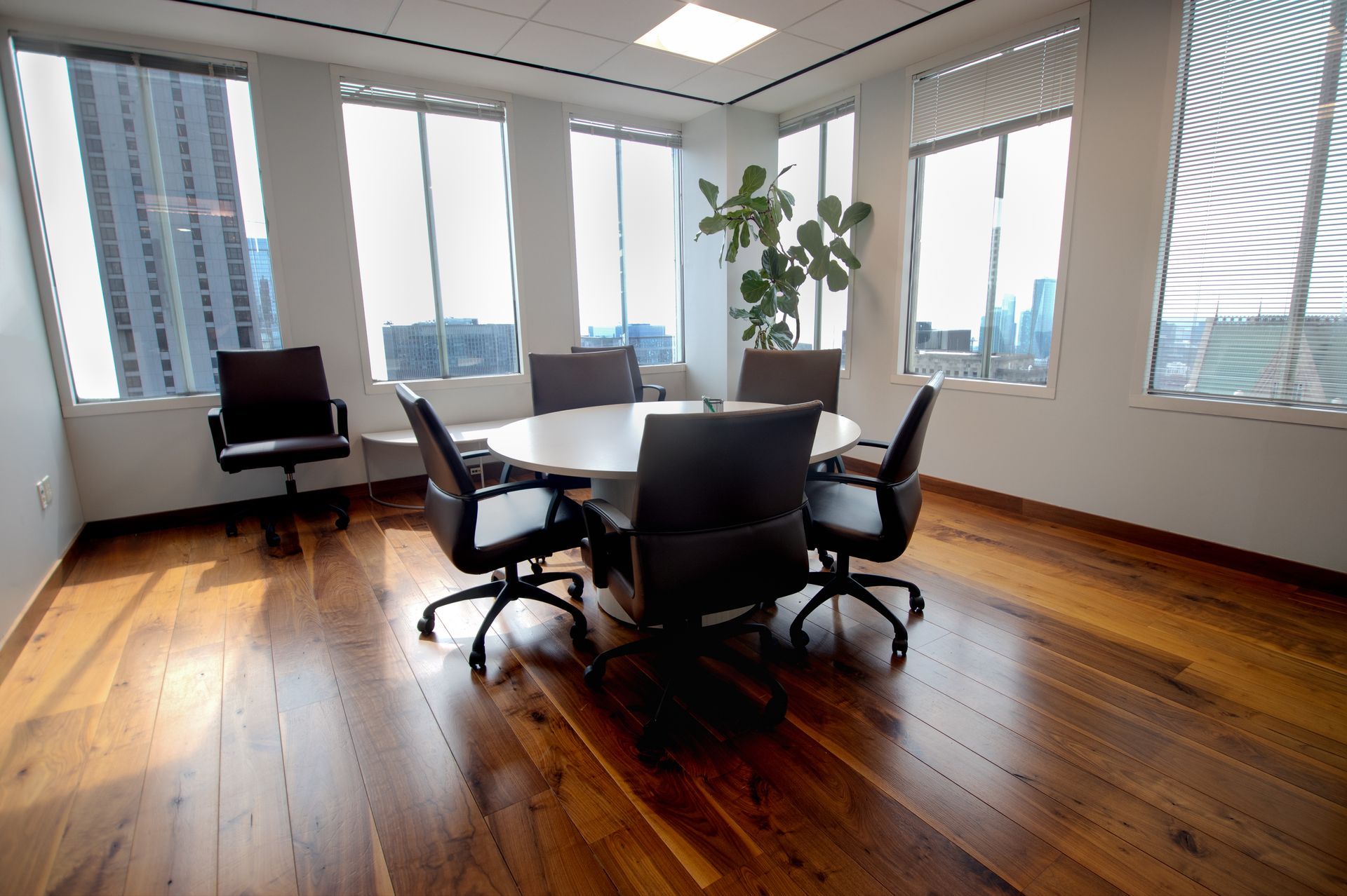 Conference room with round table, office chairs, large windows, and a hardwood floor.