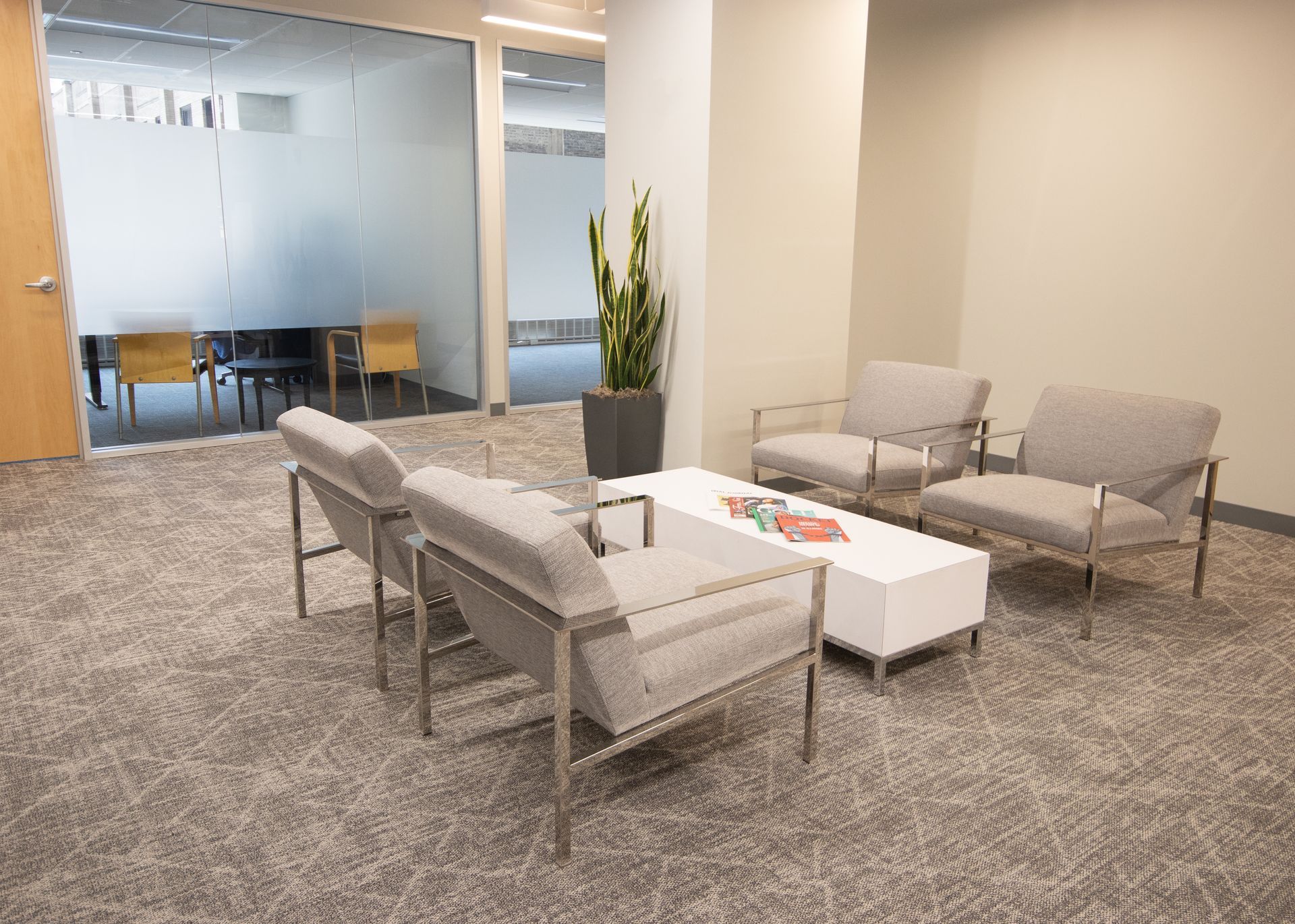 Office waiting area with four gray armchairs, a white coffee table, and a tall potted plant.