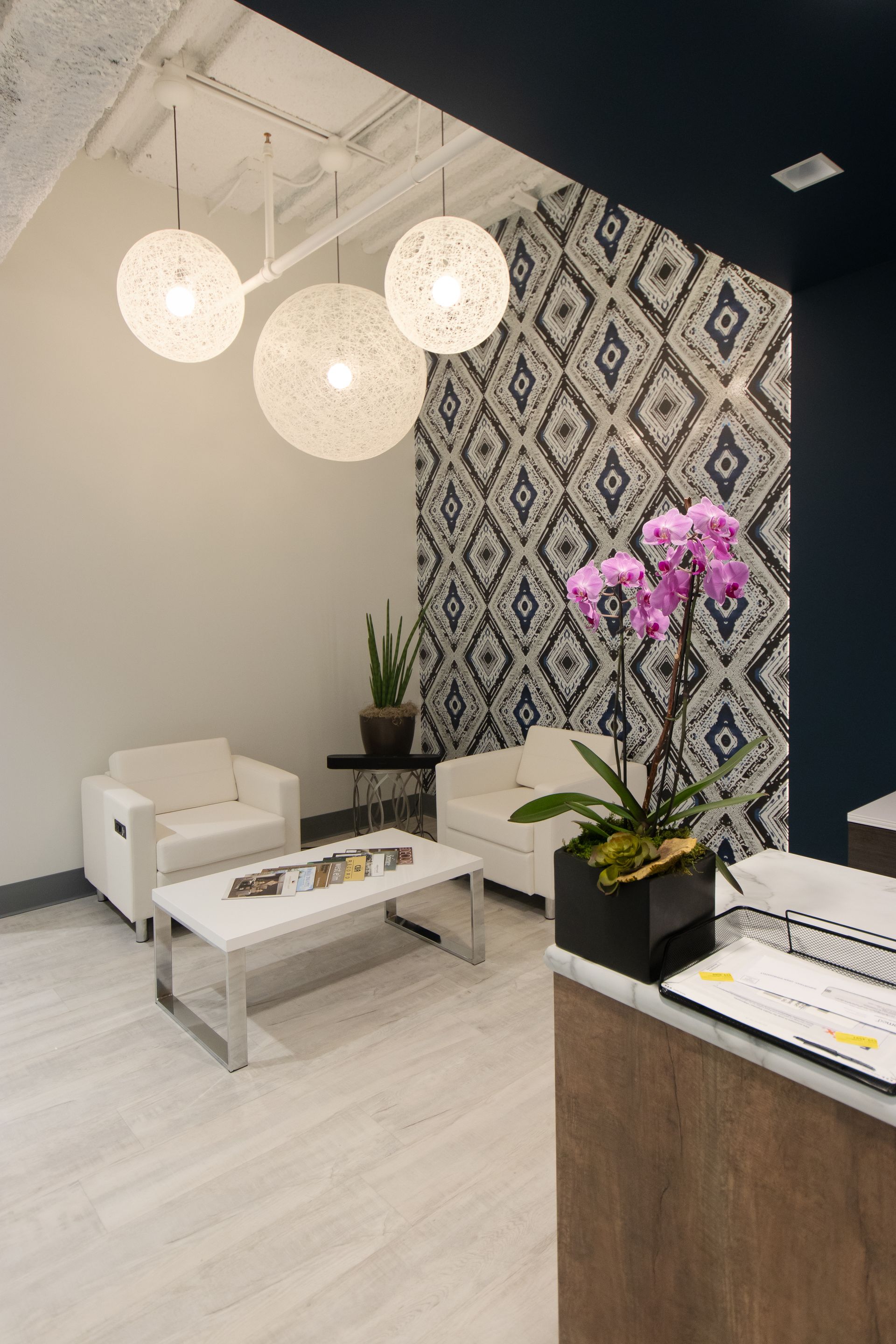 Modern waiting room with white furniture, patterned accent wall, and orchid.