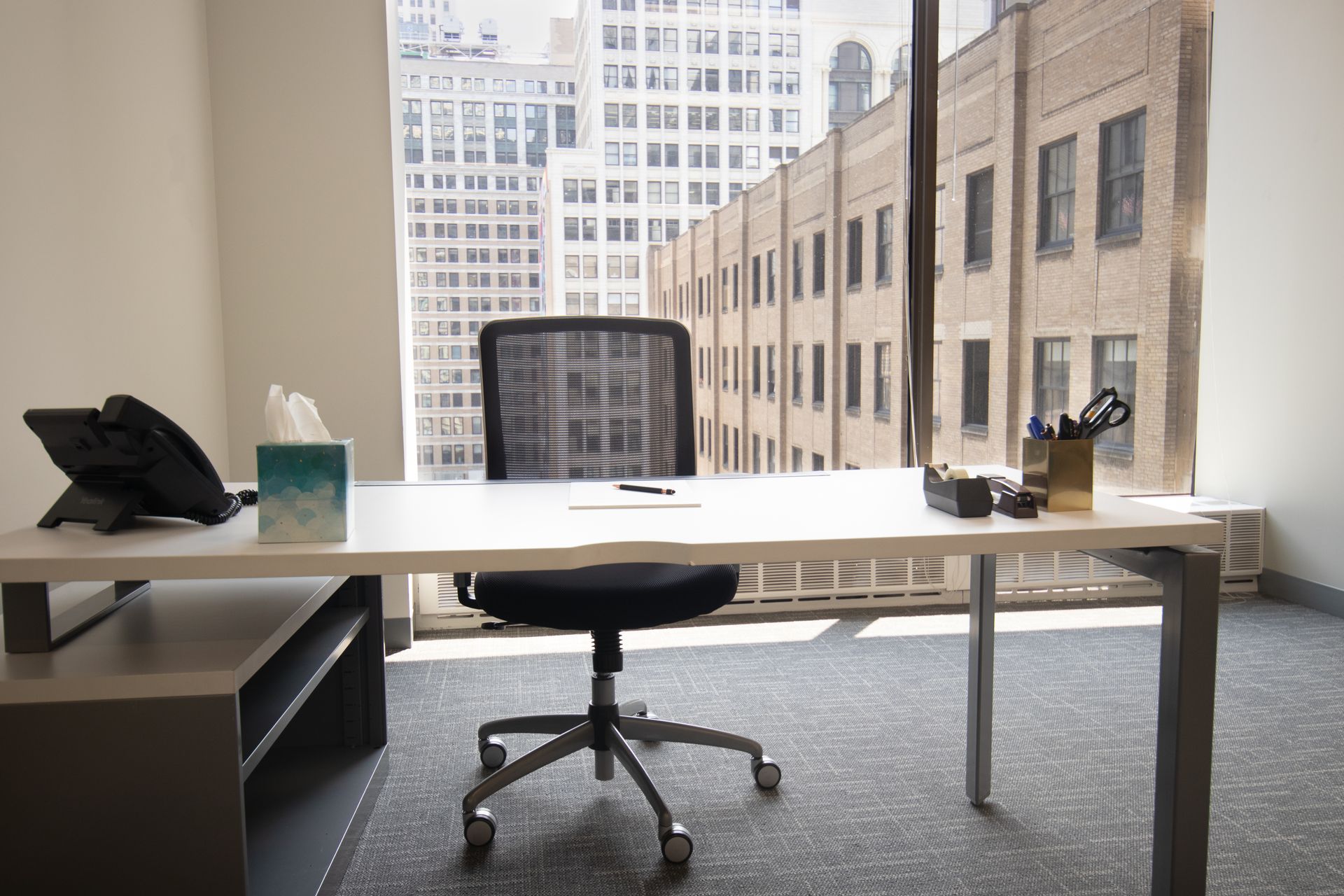 An office with a desk, chair, and window overlooking city buildings.