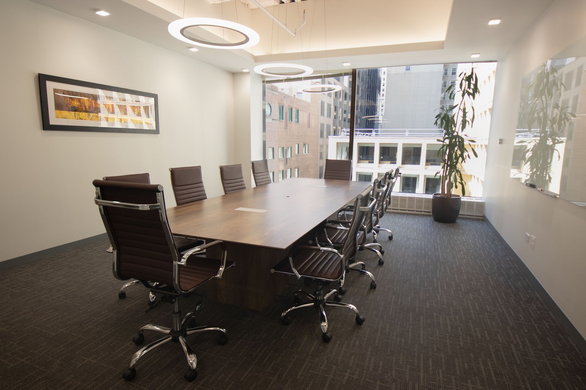 Conference room with long table, leather chairs, and large window overlooking city buildings.