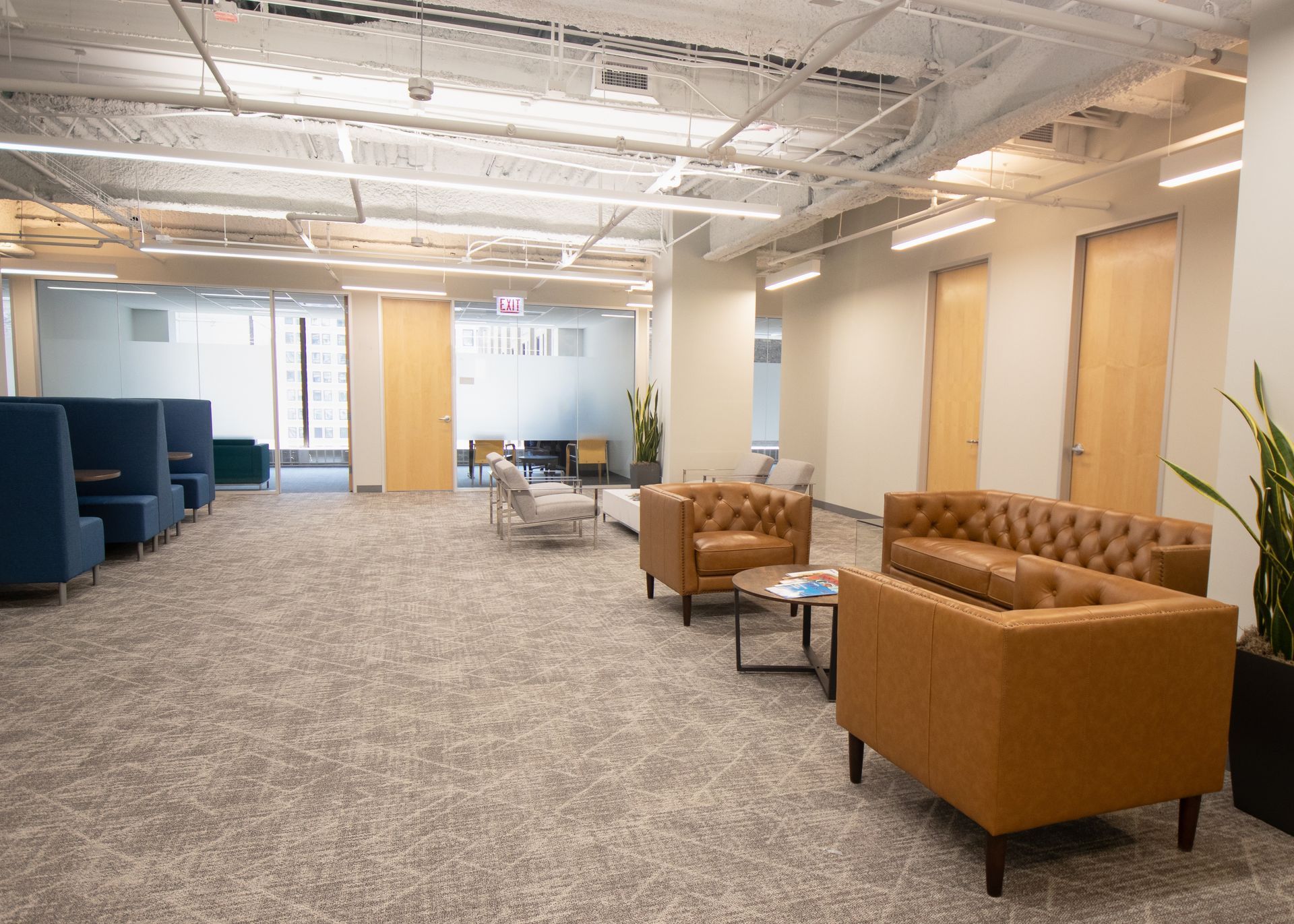 Cozy office waiting area with couches, chairs, and booths on gray carpet.