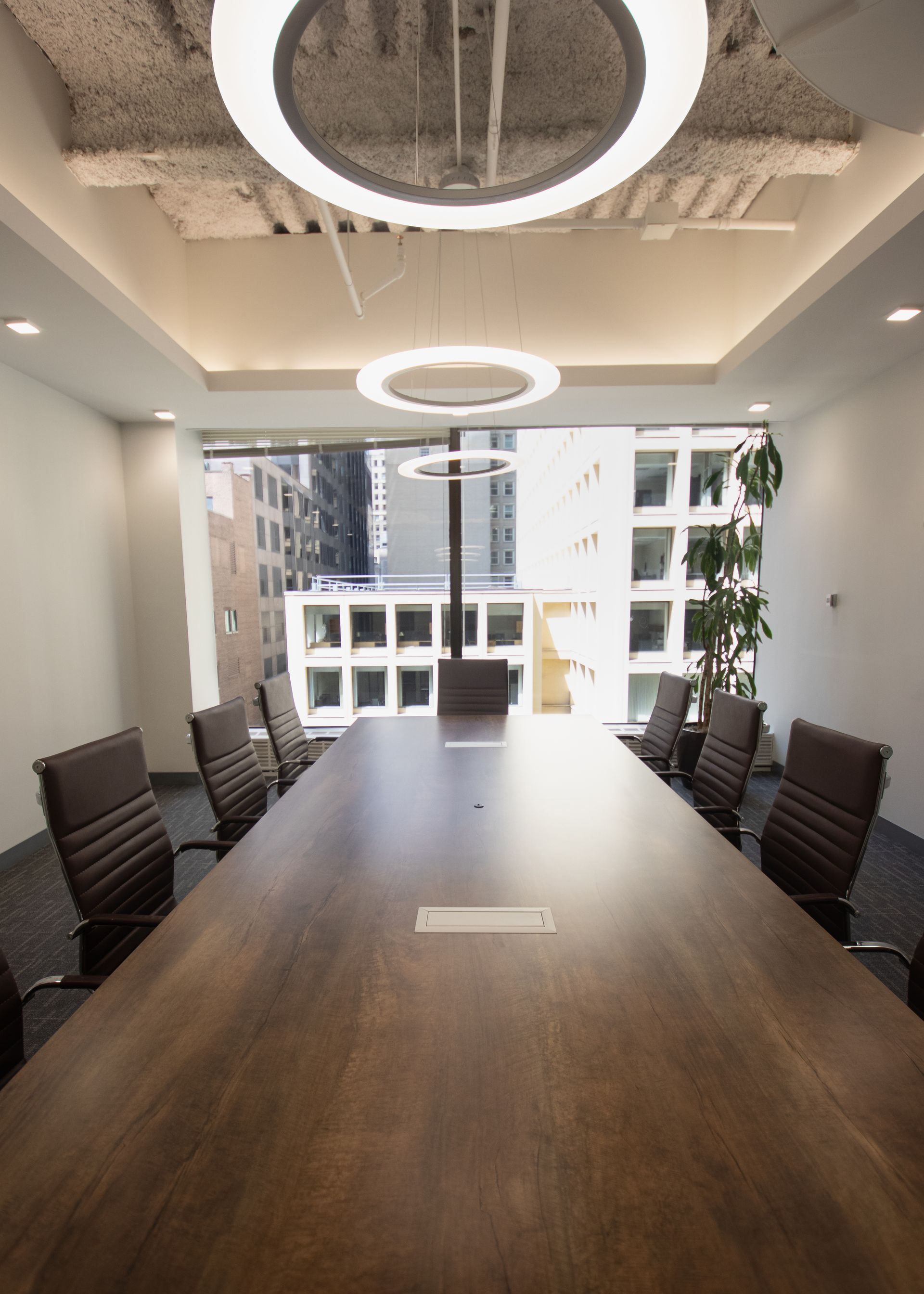Conference room with long wooden table, leather chairs, and city view through a window.