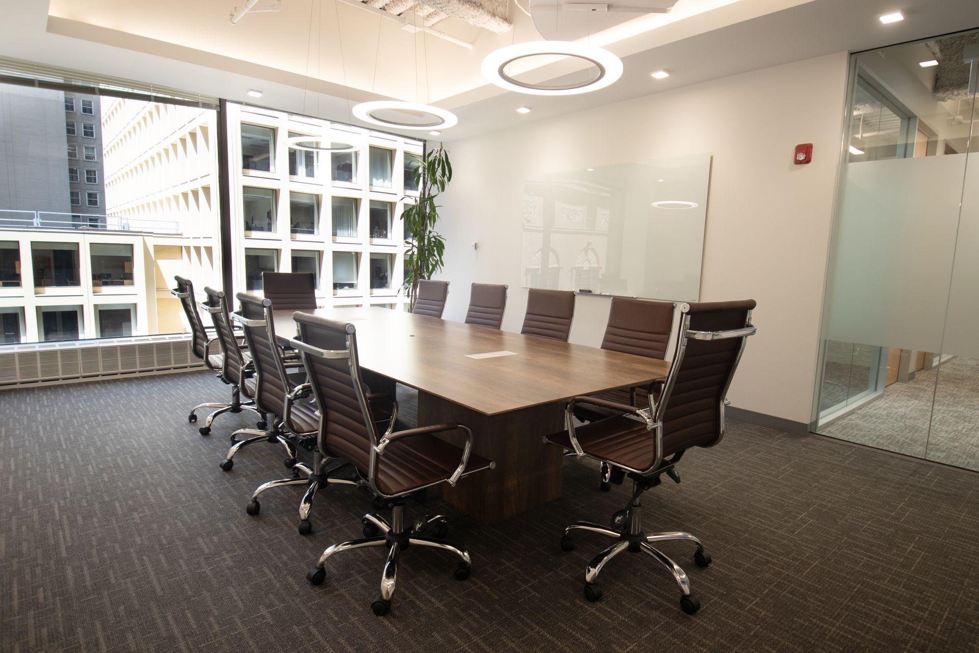 Conference room with long wooden table, brown leather chairs, and large window overlooking city.