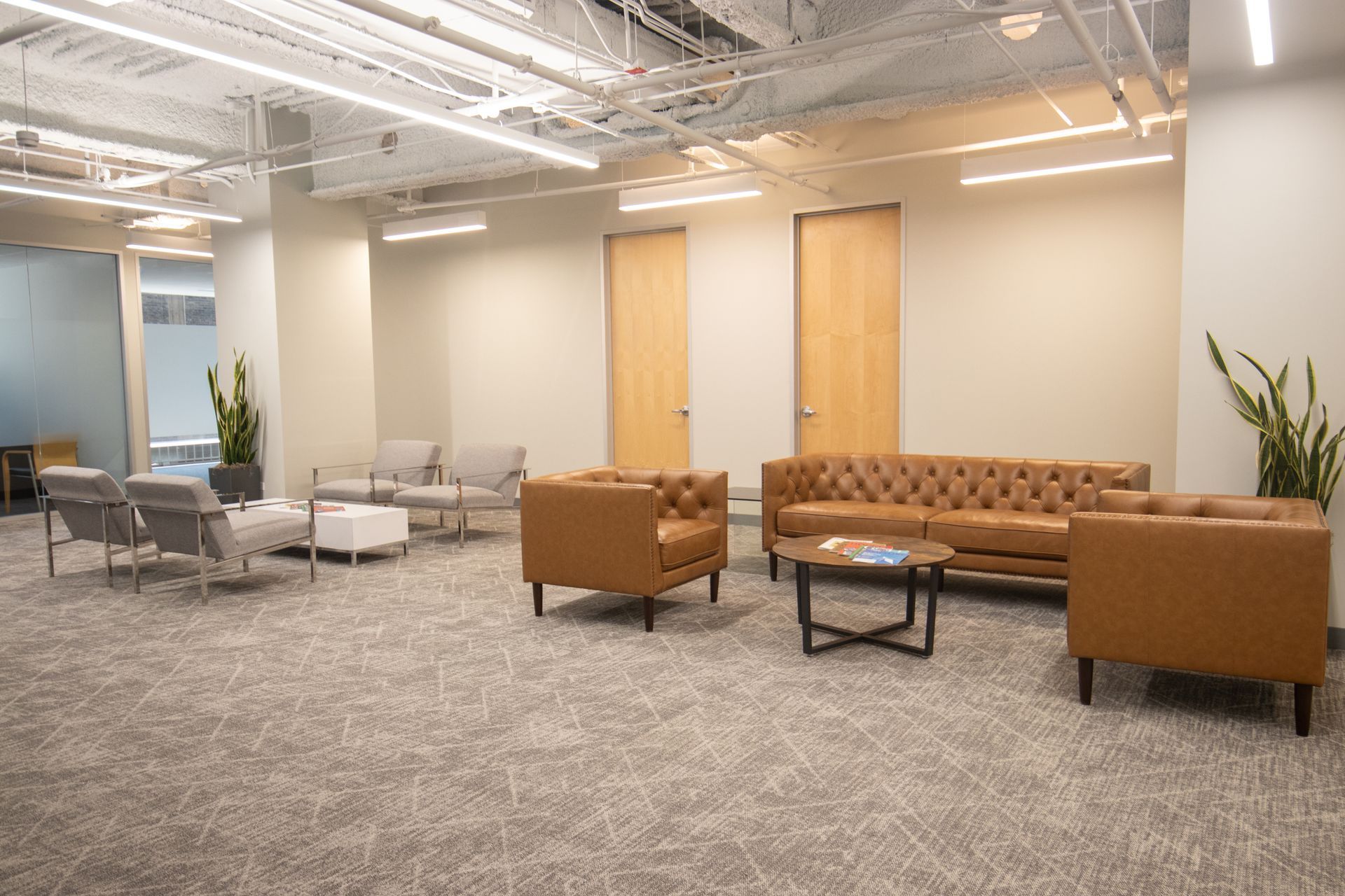 A modern waiting area with tan couches, armchairs, and chairs on a gray carpet.