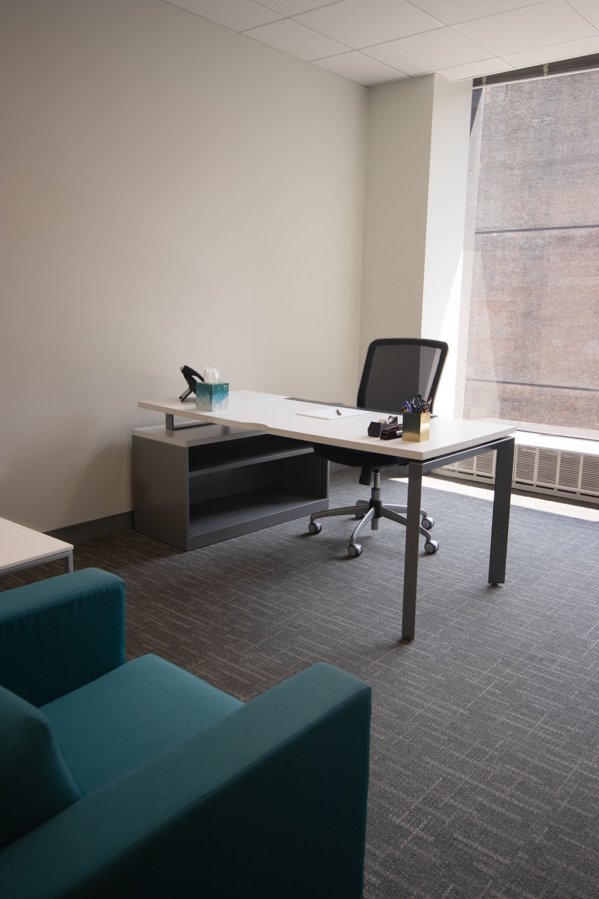 Office with desk, chair, blue accent chairs, and window with blinds.