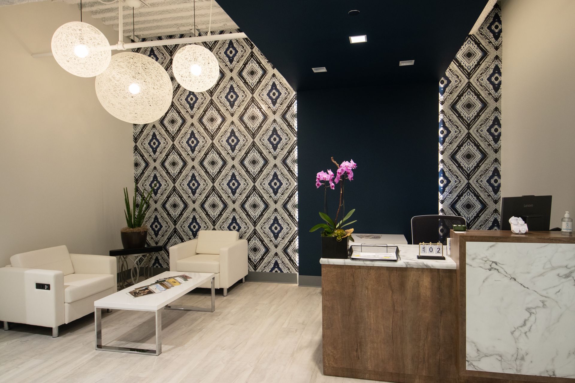 Reception area: white chairs, patterned wall, wood desk with marble, purple orchids.