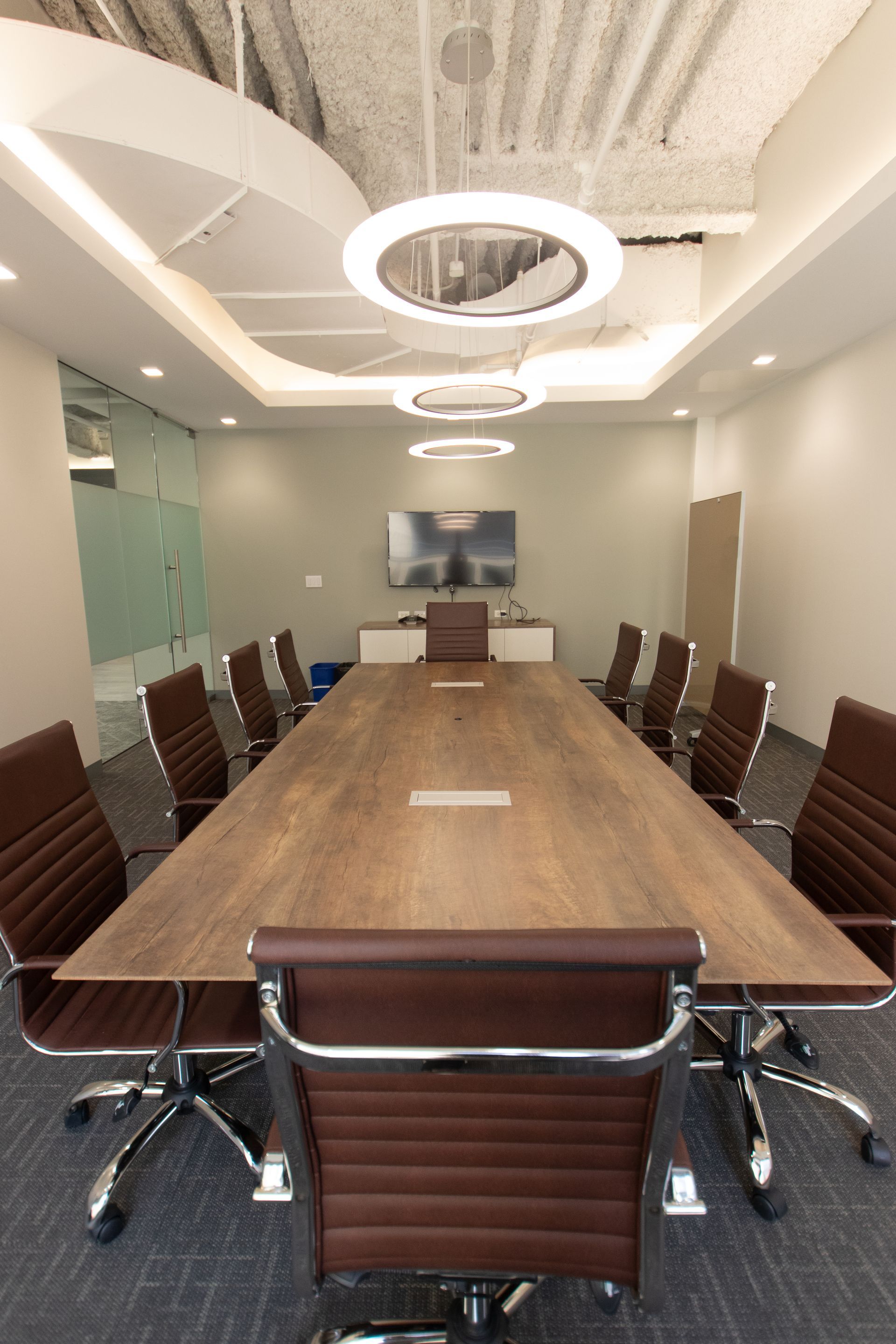 Conference room with long wooden table, brown leather chairs, and circular ceiling lights.
