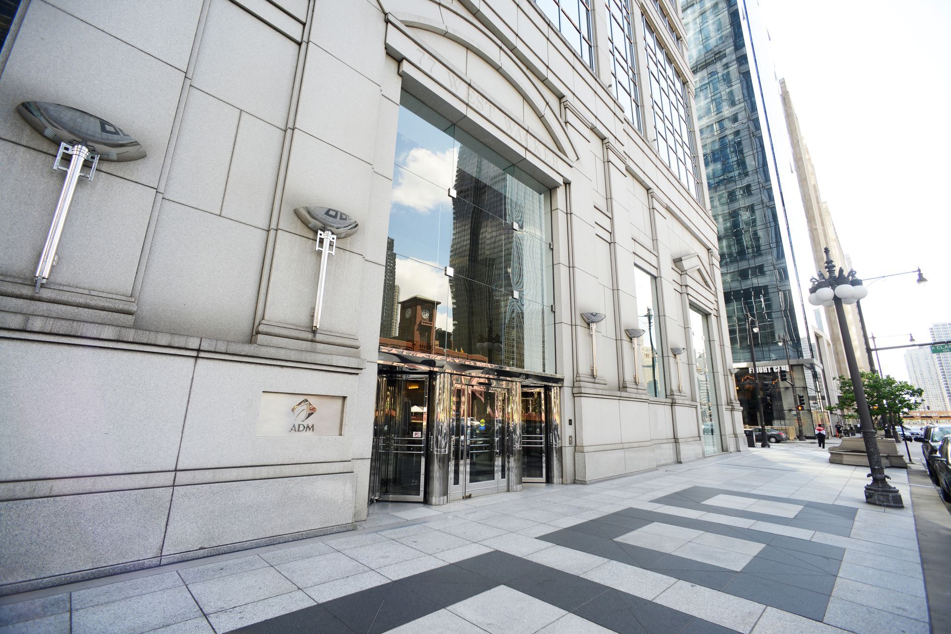 Exterior of a large, stone building with glass doors and a sidewalk along a city street.