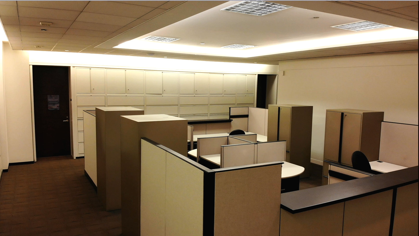Empty office cubicles in a beige and brown color scheme, with a dark brown carpet.