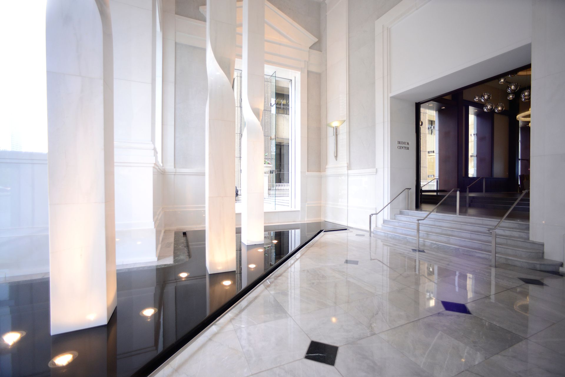 Elegant white marble lobby with dark reflective pool and pillars, doorway to interior.