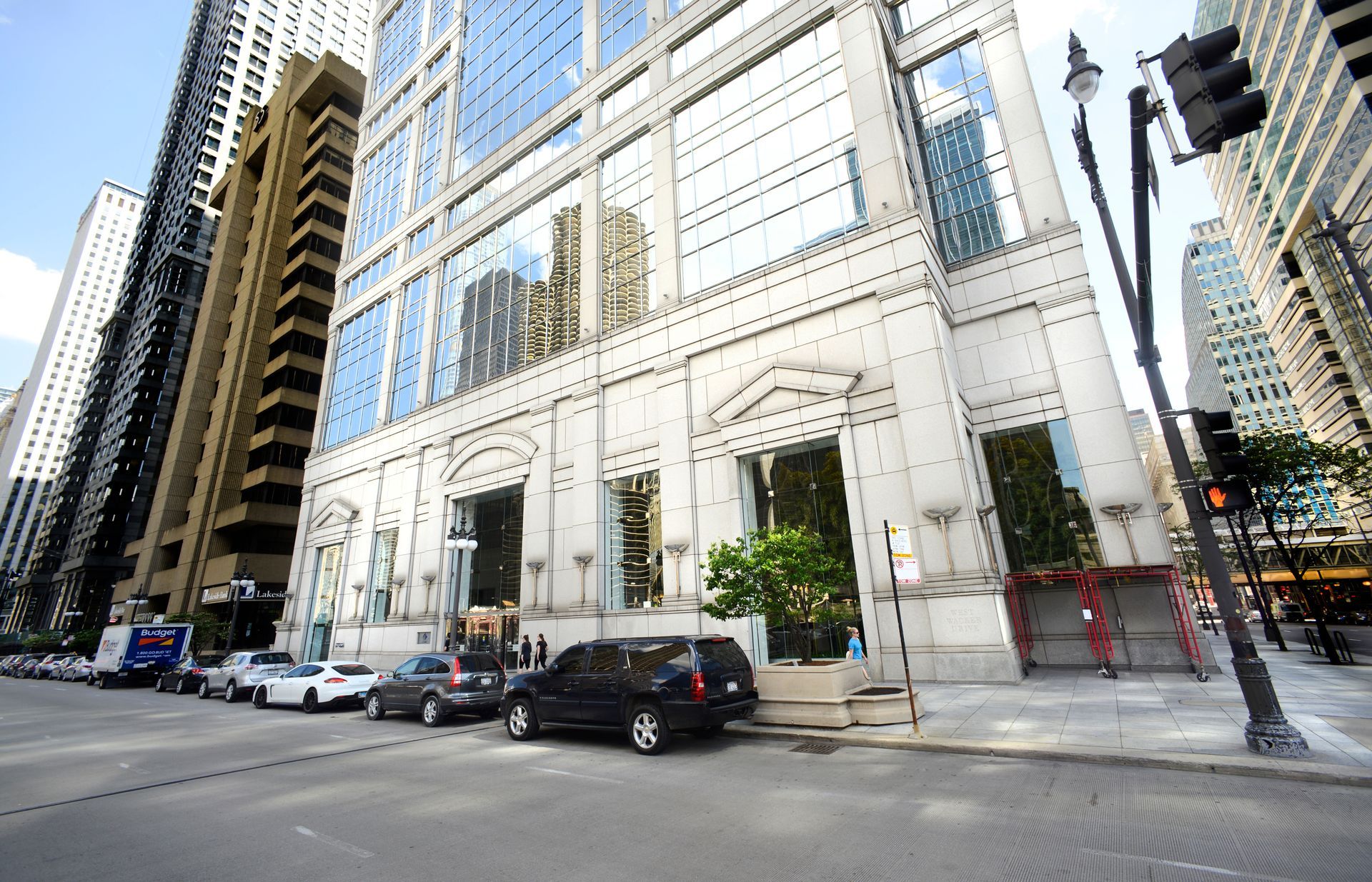 Tall white building with glass windows in a city street, cars parked along the curb.