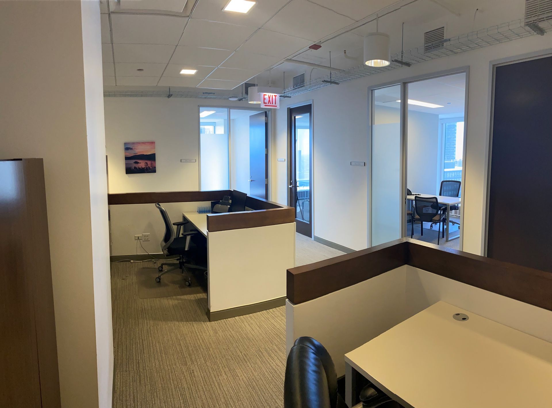 Office cubicles and glass-walled rooms; neutral color palette with carpeted floors and modern lighting.