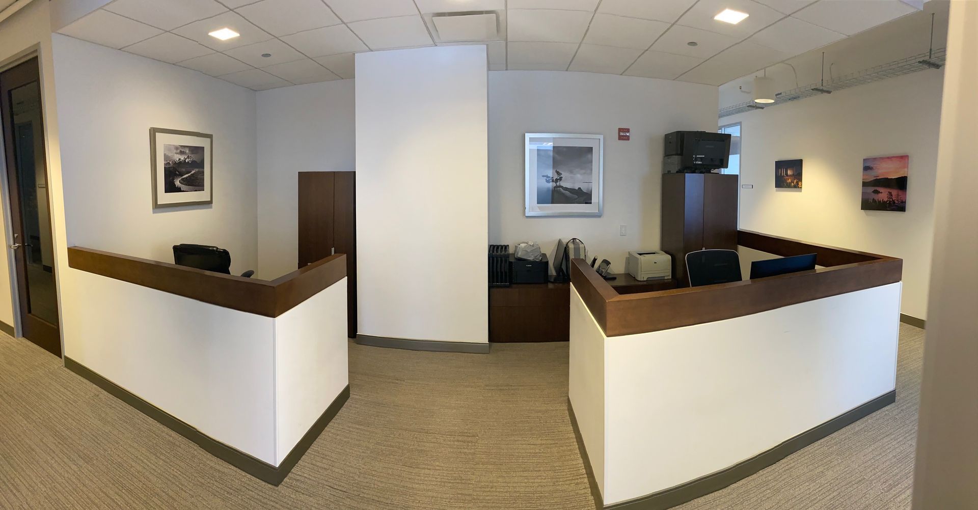 Office reception area with two brown-topped desks, art, and a large white pillar.
