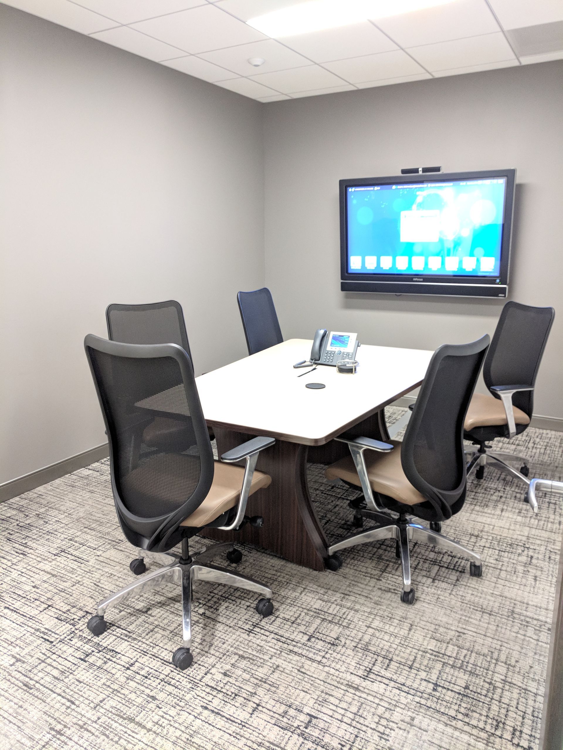 Conference room with a table, chairs, and a large screen on a wall.