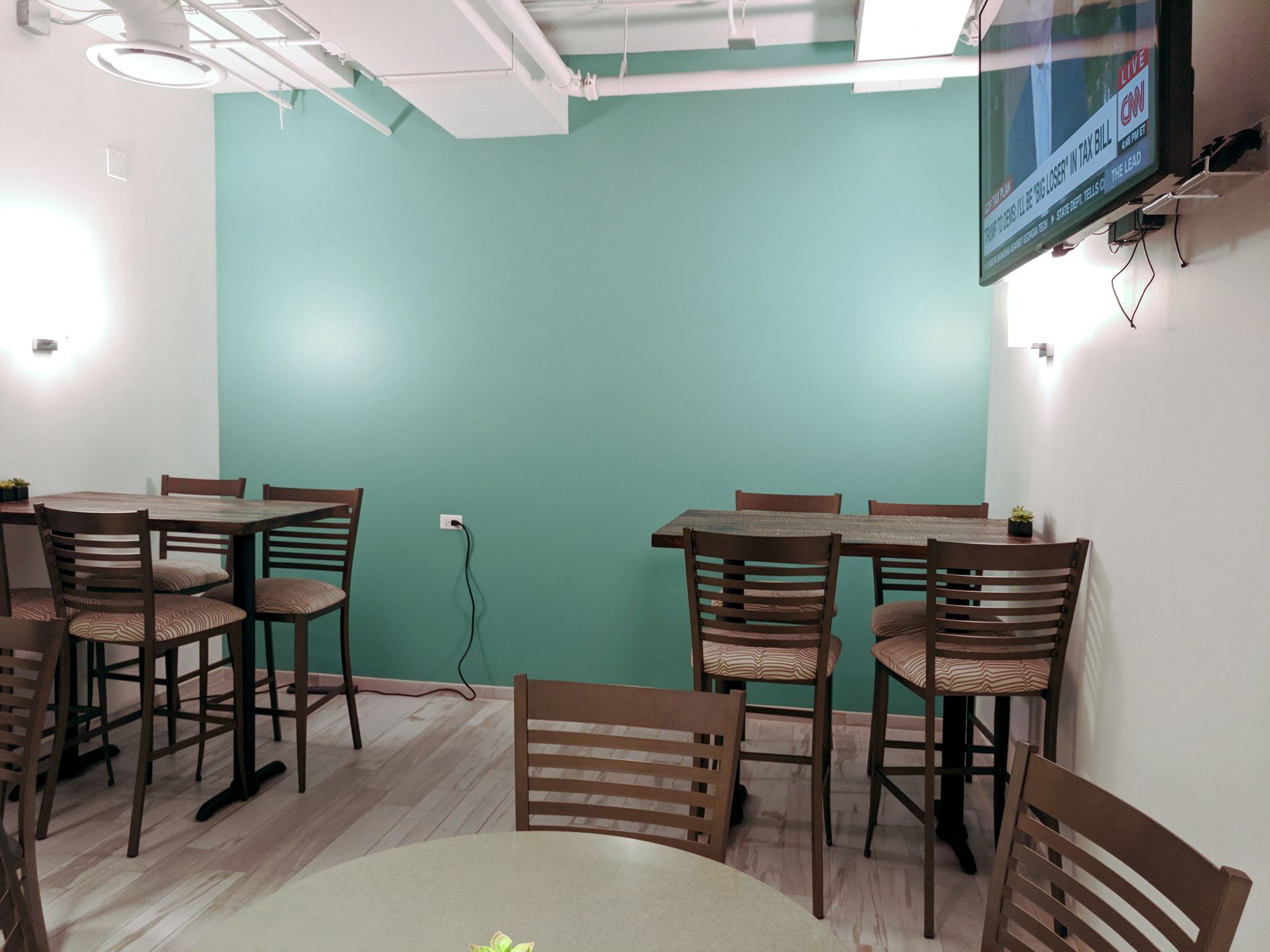 A dining area with tall chairs and tables, a TV on the wall, and a teal-colored accent wall.