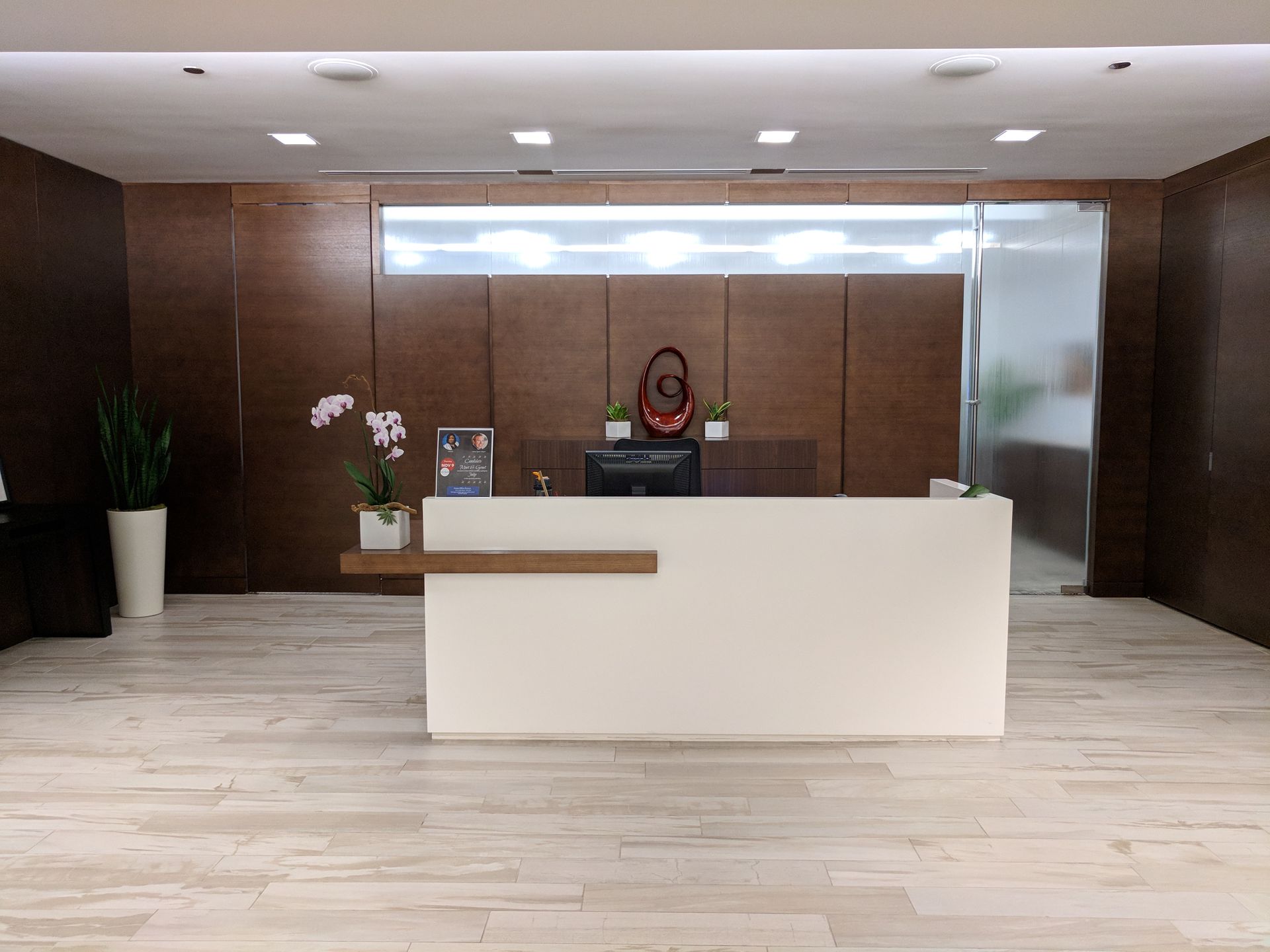 Modern office reception area with white desk, wood paneling, and plants.