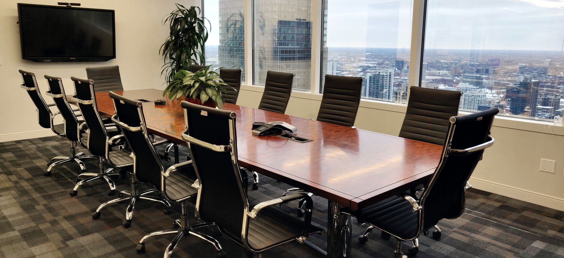 Conference room with a large wooden table, chairs, and a cityscape visible through the windows.
