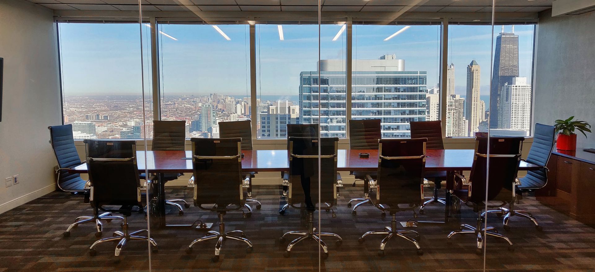 Conference room with large windows overlooking a city skyline. A long table and chairs are in the room.