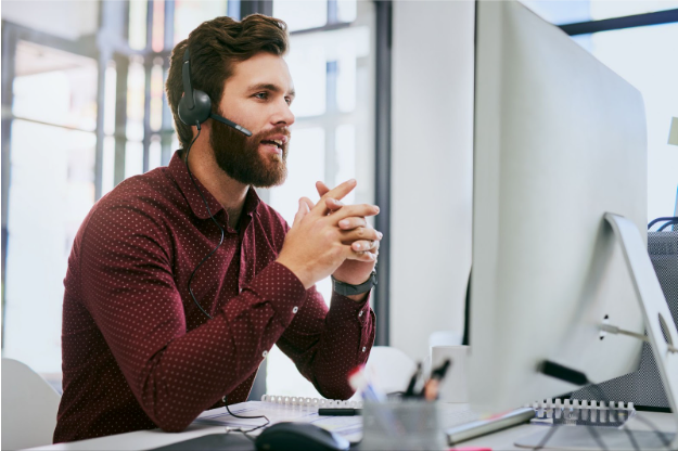 Man with headset in front of computer, hands clasped, in office setting.