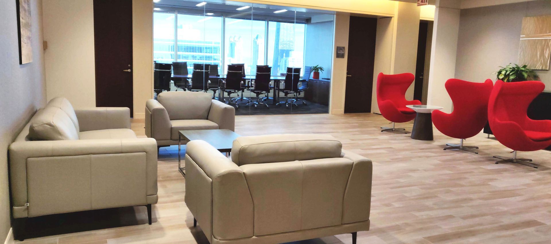 Office waiting area with couches, red chairs, and a conference room visible through a glass wall.