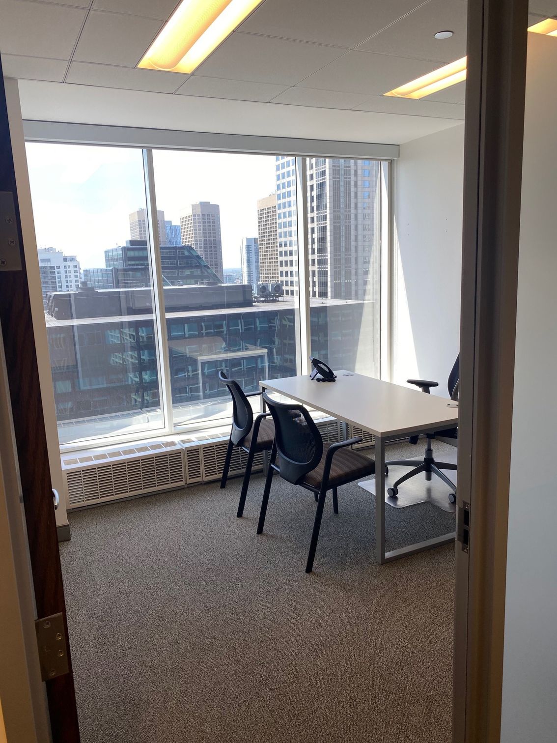An office with a table, chairs, and a large window overlooking city buildings.