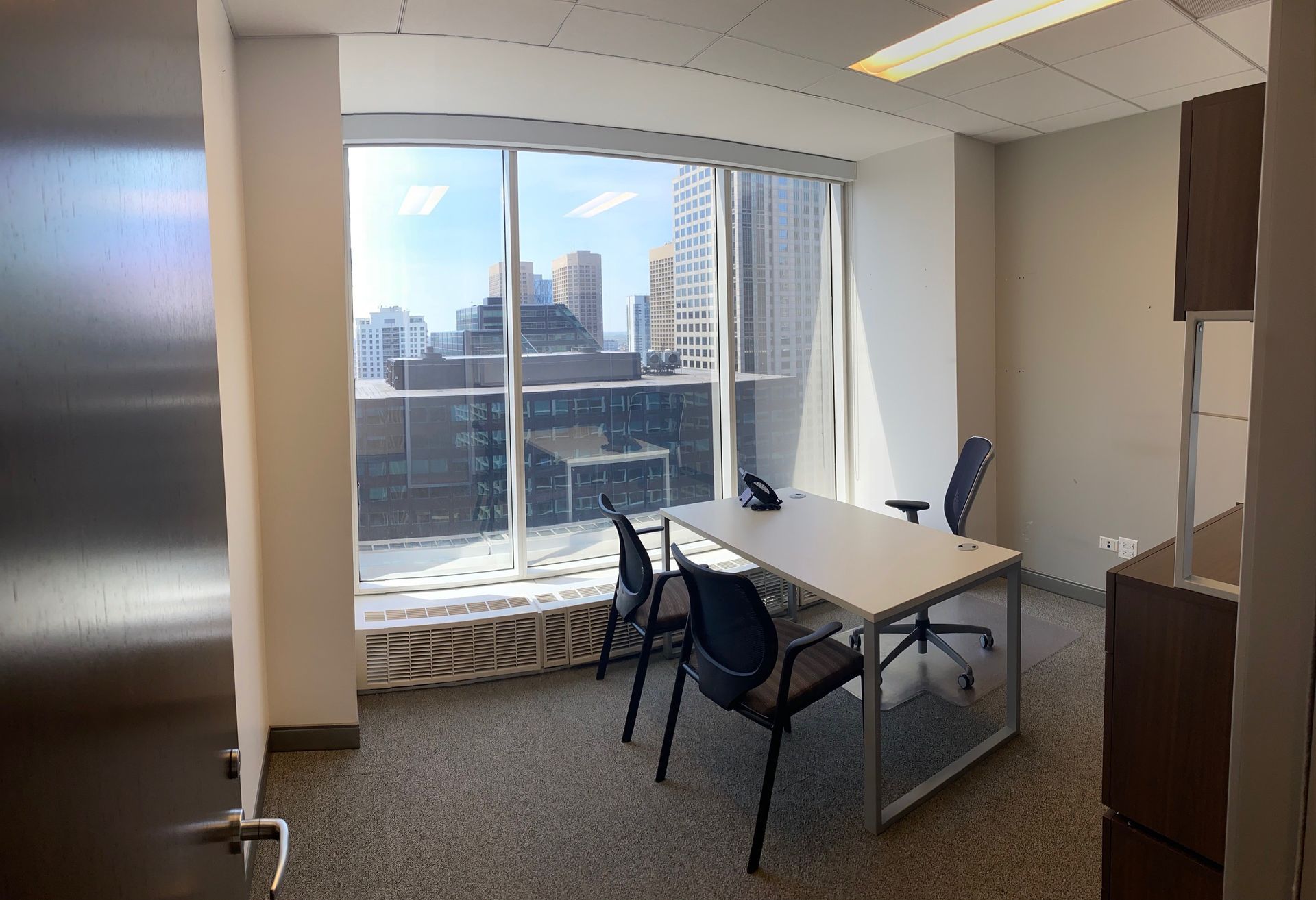 Office room with a table, chairs, and a large window overlooking city buildings.