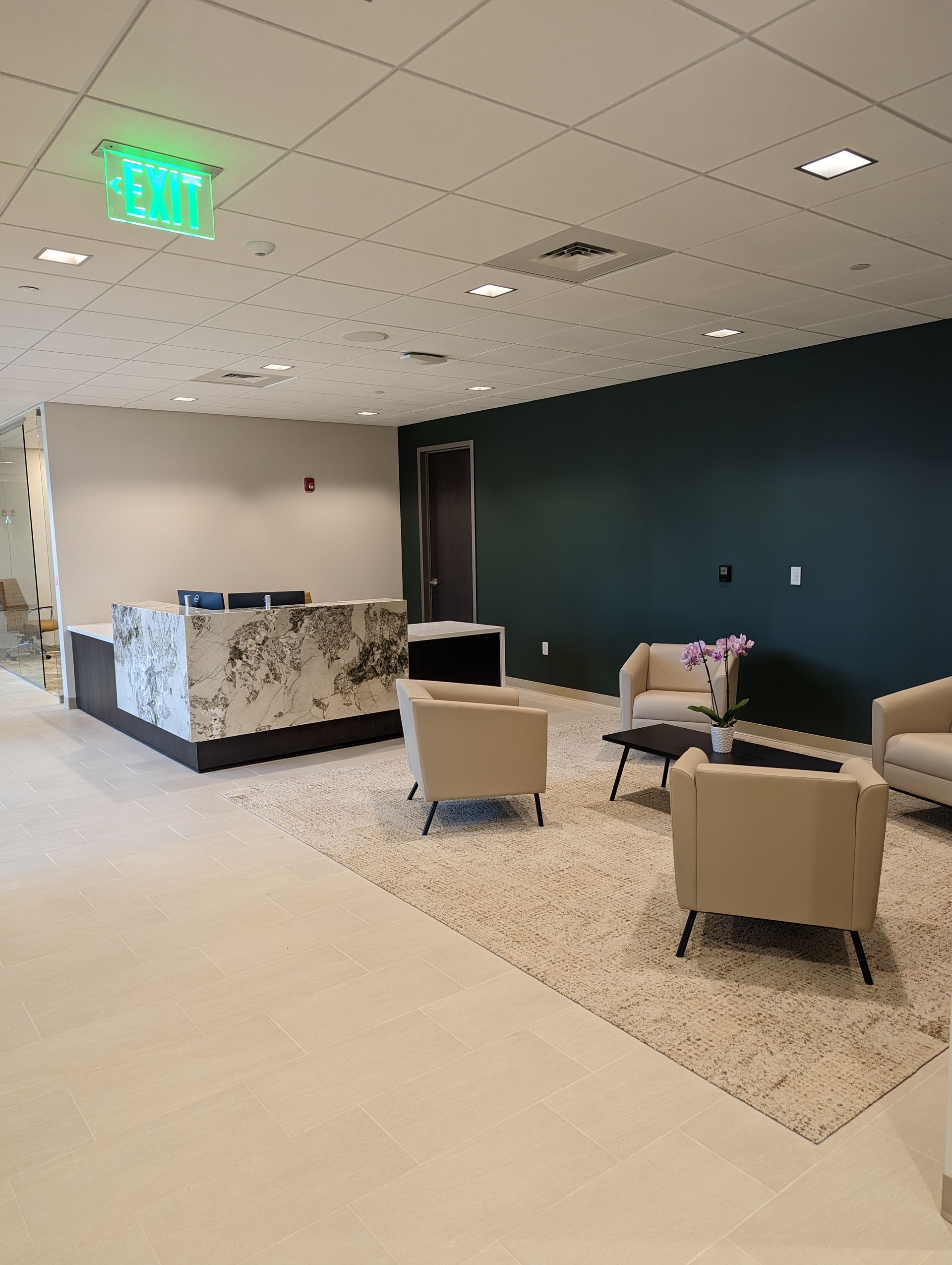 Modern office waiting area: reception desk, seating area with cream armchairs, teal accent wall, and neutral rug