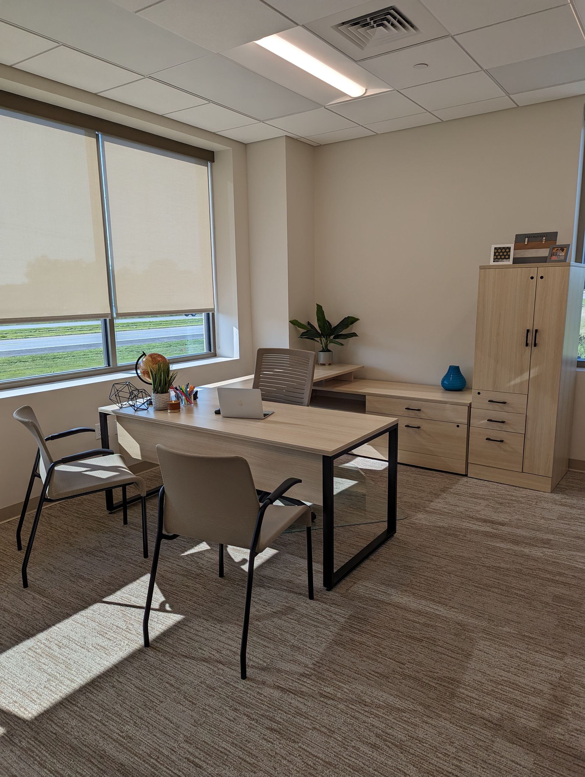 Office interior with desk, chairs, window with blinds, and cabinet. Neutral tones.