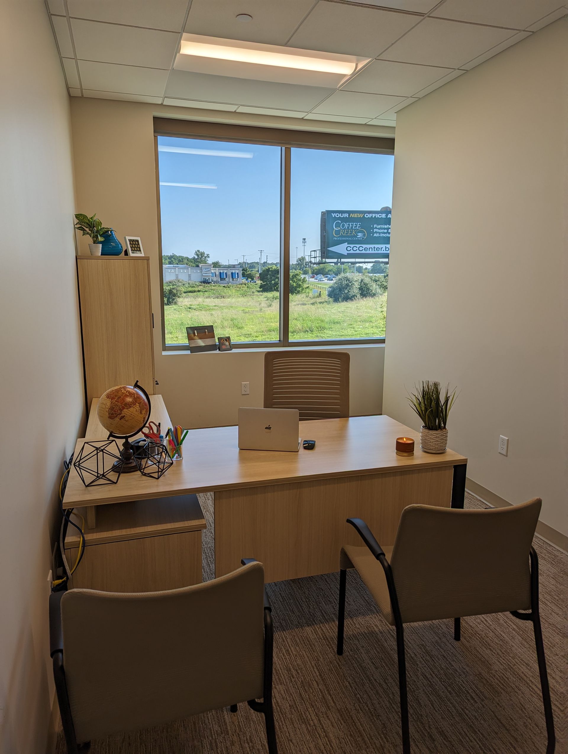 Office with desk, chairs, and window overlooking a field.