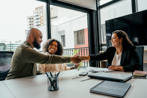 Two people shaking hands at a table in an office, with a woman smiling.