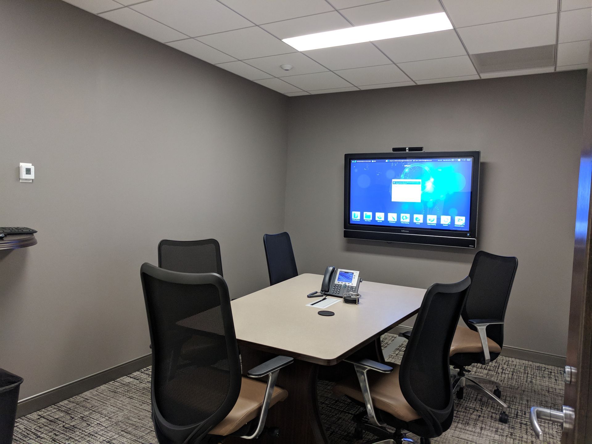 Conference room with table, chairs, large screen, and phone on the table.