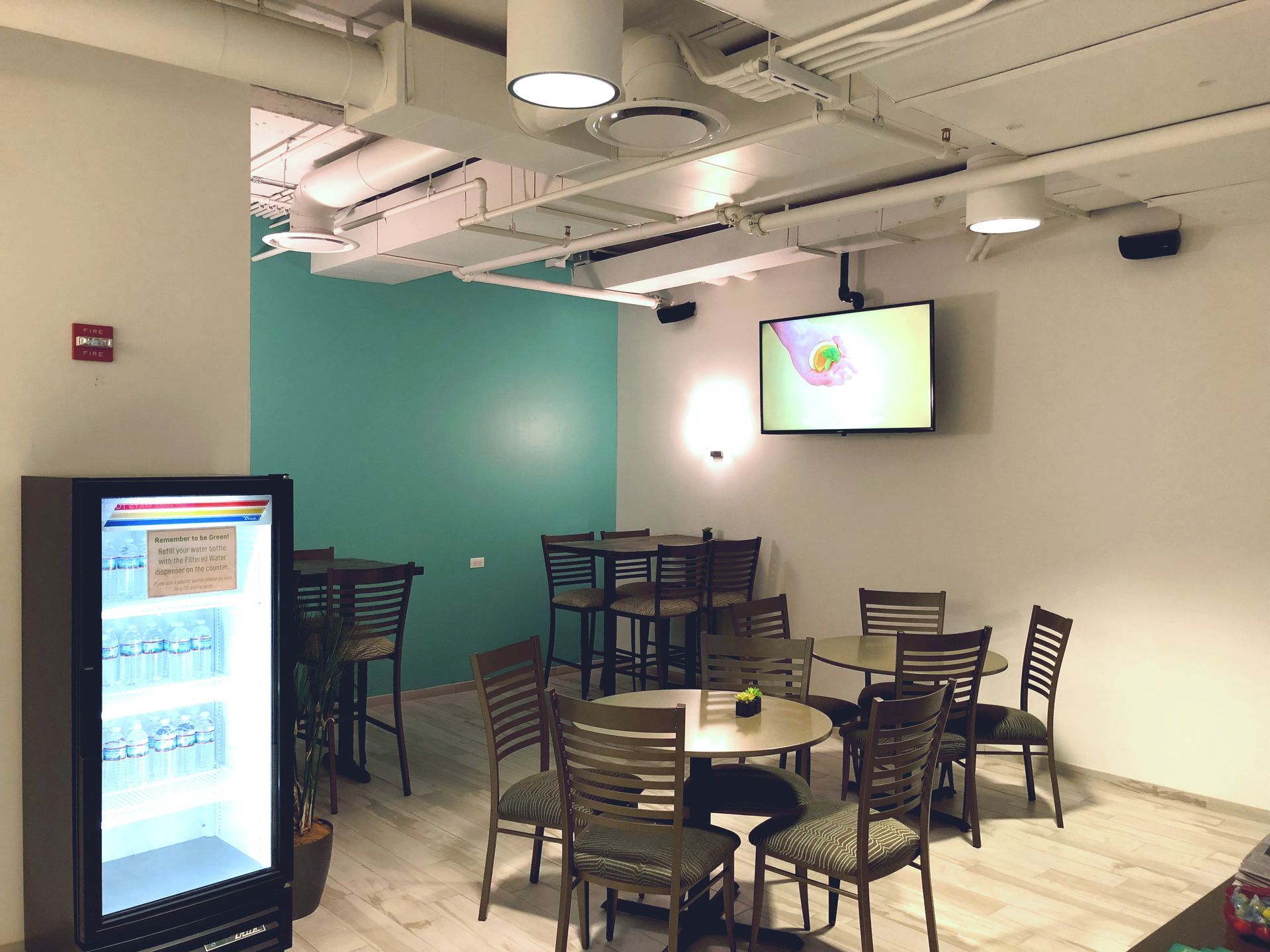 Interior of a cafe with tables, chairs, refrigerator, TV, and turquoise accent wall.